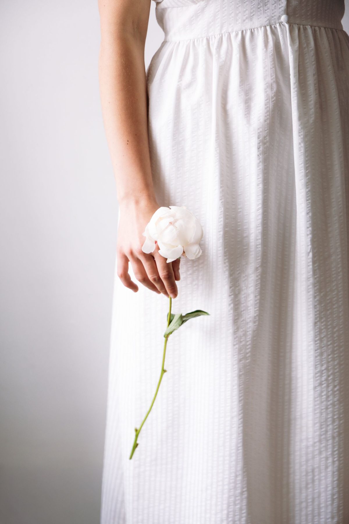 Elegant minimalist white dress with flower. Photo by Tanita Lupa